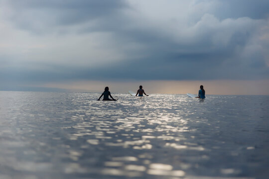 Rear view of female friends surfing in sea against cloudy sky