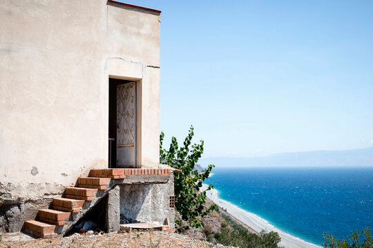 House on mountain by sea against clear sky during sunny day