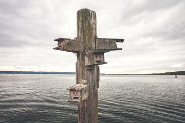 Birdhouse on wooden post by lake against cloudy sky