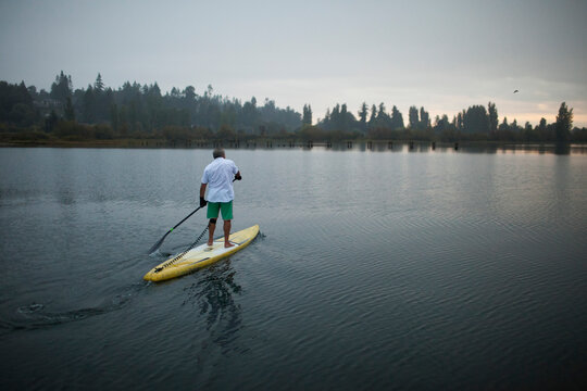 Full length of senior man paddleboarding on lake during sunset