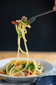 Close-up of fork with cooked bucatini over bowl on table against black background