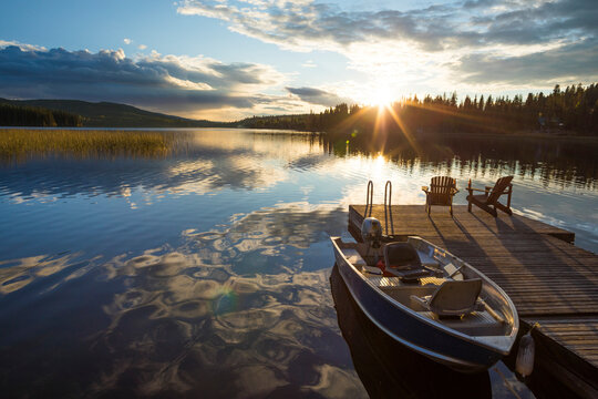 Boat moored by wooden pier on lake against cloudy sky during sunset