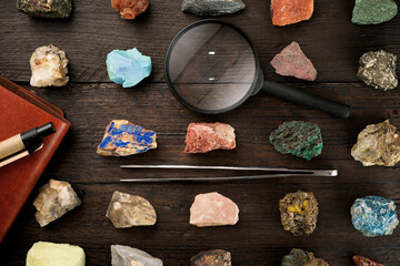 Overhead view of colorful gemstones with magnifying glass and tweezers on wooden table