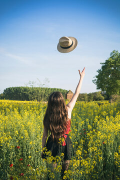 Rear view of teenage girl throwing hat while standing on field against blue sky during sunny day