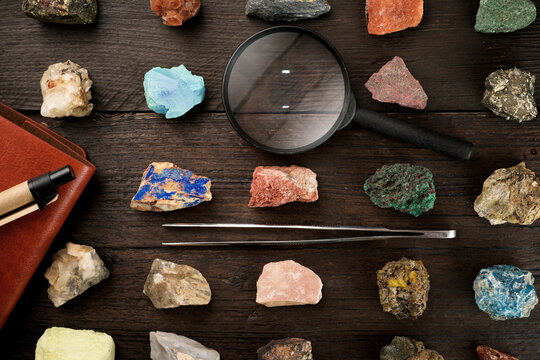 Overhead view of colorful gemstones with magnifying glass and tweezers on wooden table