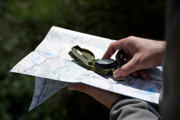 Cropped hands of hiker holding navigational compass with map in forest