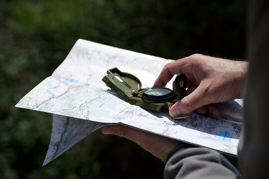 Cropped hands of hiker holding navigational compass with map in forest