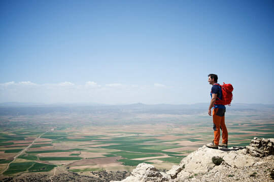 Side view of man with backpack looking at view while standing on mountain against sky during sunny day