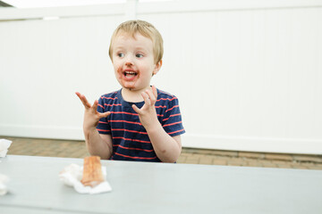 Boy with messy mouth dropped ice cream cone on table against wall