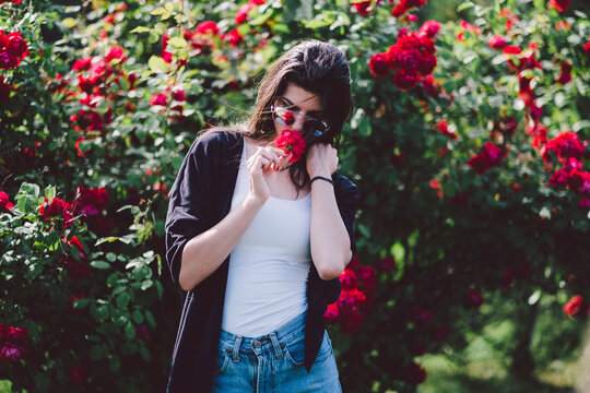 Woman in sunglasses smelling flower while standing by plants at park