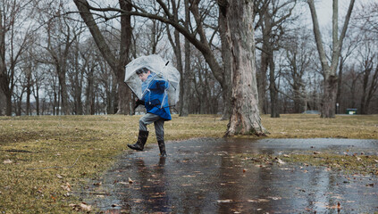 Boy holding umbrella while walking on wet field during rainy season