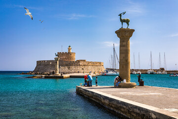 Mandraki port with deers statue, where The Colossus was standing and fort of St. Nicholas. Rhodes, Greece. Hirschkuh statue in the place of the Colossus of Rhodes, Rhodes, Greece - obrazy, fototapety, plakaty