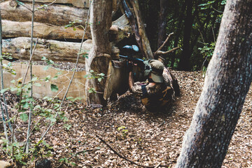 Army solider aiming gun while lying on field in forest during training
