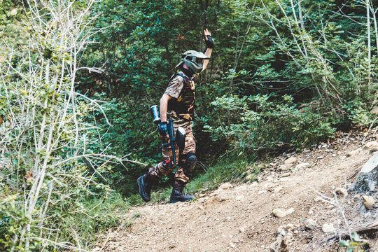 Side view of army solider with gun waving hand while walking on hill in forest