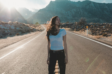 Young woman with eyes closed standing on road against mountains during sunny day