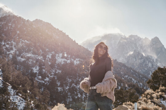 Low angle view of smiling young woman standing against mountains during sunny day