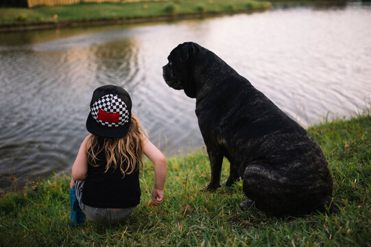 Rear view of girl crouching by black dog on riverbank at park