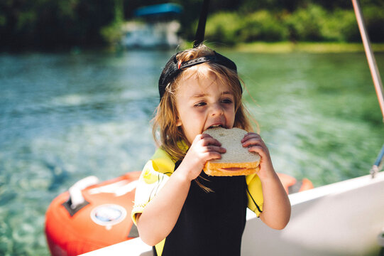 Cute girl biting sandwich against river at park