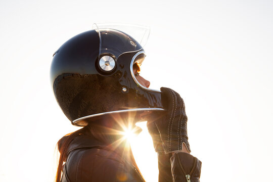 Side view of female biker adjusting helmet against clear sky during sunset