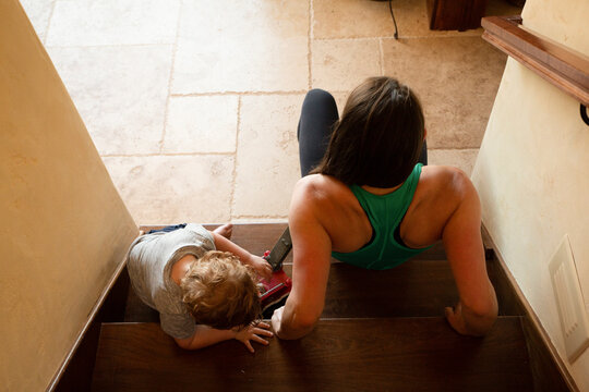 High angle view of mother exercising while son playing with toy crane on wooden steps at home
