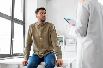 Fototapeta premium medicine, healthcare and people concept - female doctor with clipboard and male patient having health problem at hospital
