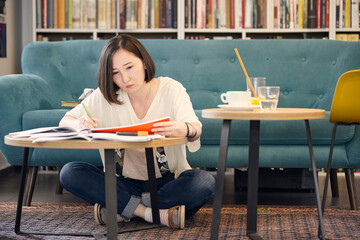 Full length of young woman studying while sitting on carpet at home
