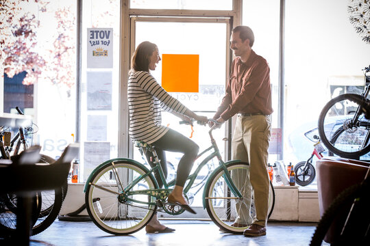Owner looking at happy female customer examining bicycle in store