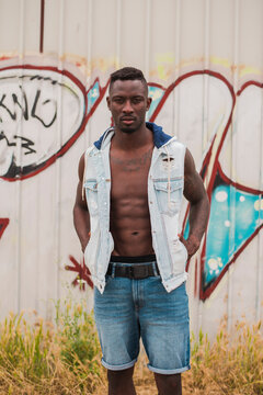 Portrait of confident young man wearing unbuttoned jacket standing on field against graffiti wall