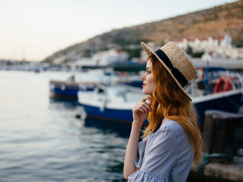 Side view of woman wearing hat looking away while standing at harbor against sky during sunset