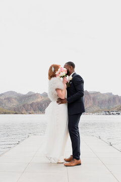 Full length side view of newlywed couple with bouquet standing on pier over lake