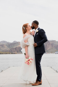 Full length side view of newlywed couple kissing while standing on pier over lake