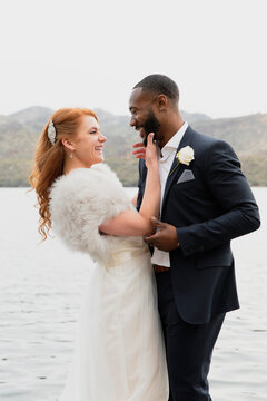 Side view of smiling wife touching husband's beard while standing against lake
