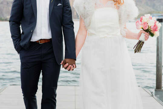 Midsection of newlywed couple holding hands while standing against lake