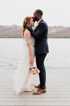Side view of loving husband kissing on wife's forehead while standing against lake