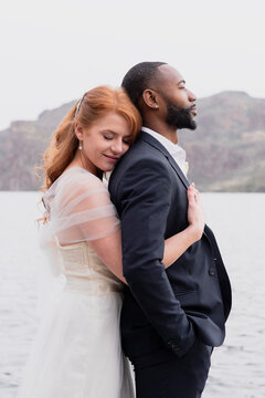Side view of wife embracing husband while standing by lake