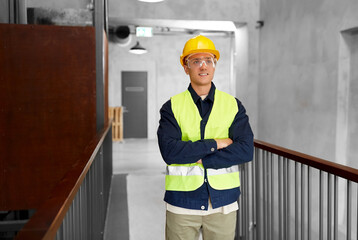 architecture, construction business and building concept - happy smiling male builder in helmet, goggles and safety west at office