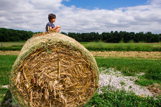 Boy looking at view while sitting on hay bale against cloudy sky