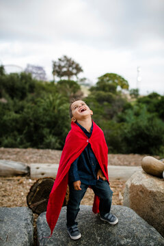 Happy boy wearing red cape while standing on rock against cloudy sky at park