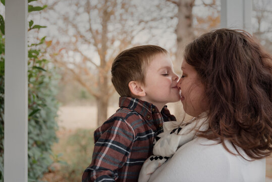Close-up of son kissing mother on nose against trees in porch