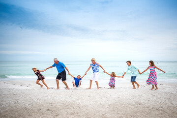 Full length of grandparents and grandchildren holding hands while playing at beach against sea and sky