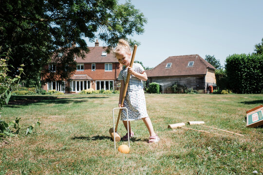 Happy girl playing croquet on grassy field at yard against clear sky during sunny day