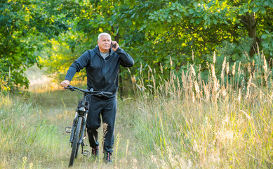 an elderly sports man uses a smartphone while walking on a bicycle
