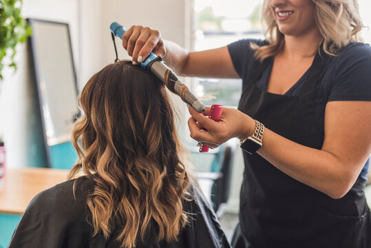 Midsection of hairdresser using curling tongs on customer's hair in salon
