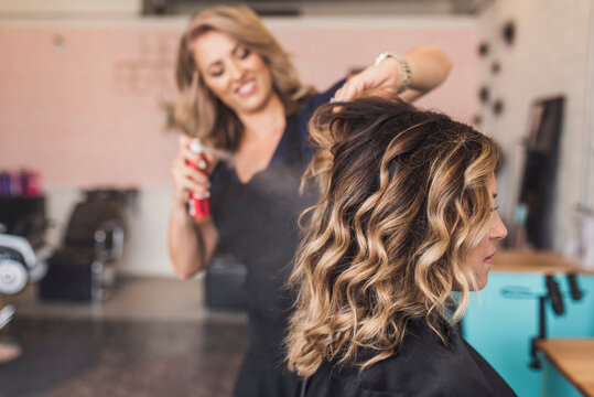 Hairdresser spraying beauty product on customer's wavy hair in salon