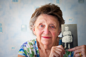 Portrait of senior woman showing her childhood photograph against wall at home