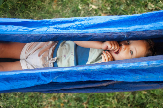 High angle portrait of cute girl sucking thumb while lying in hammock at backyard