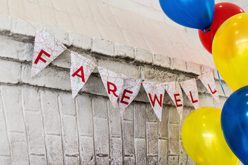 Farewell text on buntings by colorful helium balloons hanging against wall