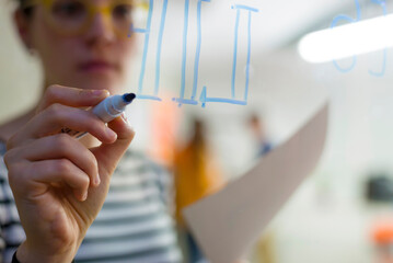 Close-up of businesswoman writing on window in creative office seen through glass