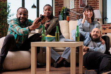 Cheerful people having fun playing video games strategy at house party with bottles of beer and snacks. Group of friends celebrating hangout reunion while they play game on tv console.