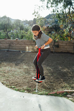 Girl jumping with pogo stick against sky in park during sunny day